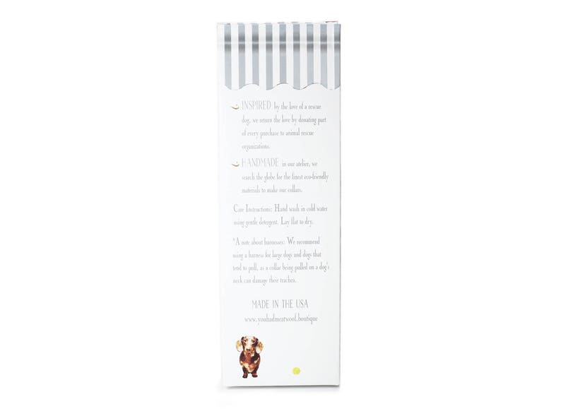 May include: A white rectangular product box with a gray striped design at the top. The box features text about the product's inspiration, handmade nature, and care instructions. A dachshund illustration is at the bottom.