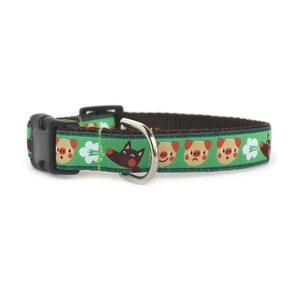 Puede incluir: Un collar para mascota de color verde con un patrón repetitivo de caras de cerdo de dibujos animados con varias expresiones, formas de nubes blancas y cabezas de lobo marrones. Incluye una hebilla de plástico negra y una anilla de metal plateado.
