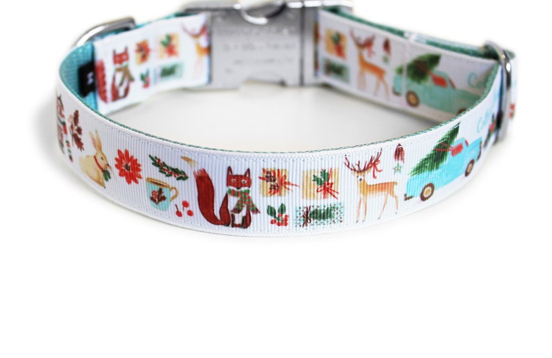 May include: White dog collar with a festive holiday design. The collar features illustrations of a fox, deer, gifts, and a blue truck carrying a Christmas tree. The collar has a teal backing and a silver metal clasp.