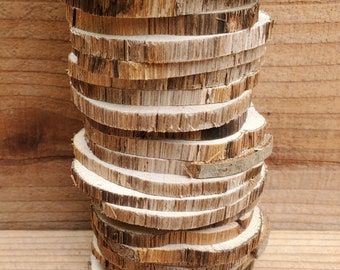 May include: A stack of wooden rounds, each with a natural bark edge, arranged in a vertical column. The wood is a light brown color with darker brown streaks.
