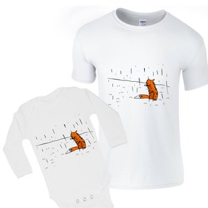 Pode incluir: Um body branco de manga comprida e uma camiseta branca de manga curta com uma ilustração preta e laranja de uma raposa sentada na chuva.