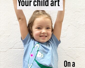 以下が含まれることがあります： 小さな子供が、頭の上に赤い丸がある緑色の生き物の絵を掲げています。絵は「Your child art」という文字が印刷された白い紙に描かれています。子供は、頭の上にピンクの丸がある緑色の生き物と「Nova」という文字が印刷された薄い青色のTシャツを着ています。