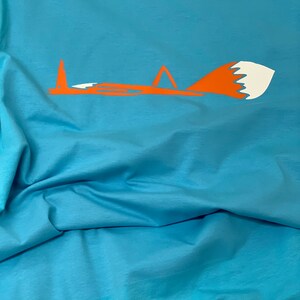 K&ouml;nnte beinhalten: Ein hellblaues T-Shirt mit einem stilisierten orangefarbenen Fuchsdesign. Der Fuchs schaut nach links und hat eine wei&szlig;e Schwanzspitze.