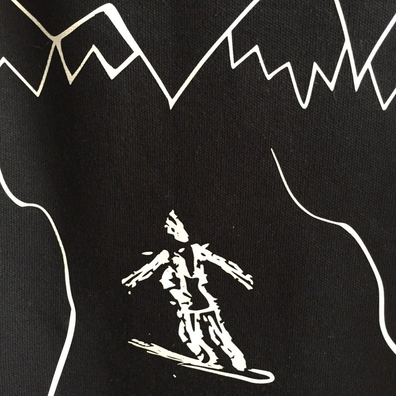 K&ouml;nnte beinhalten: Schwarz-wei&szlig;-Grafikdruck eines Skifahrers auf schwarzem Hintergrund. Der Skifahrer tr&auml;gt eine Jacke und eine Hose. Der Skifahrer f&auml;hrt einen Berg hinunter. Der Hintergrund ist ein stilisiertes Gebirge.