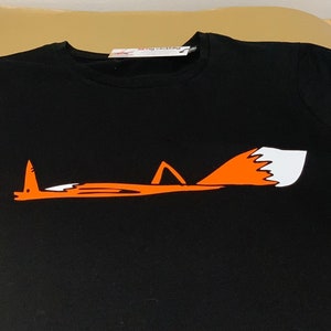 K&ouml;nnte beinhalten: Schwarzes T-Shirt mit einem orangefarbenen Fuchs-Motiv. Der Fuchs liegt mit eingerolltem Schwanz. Die Spitze des Fuchsschwanzes ist wei&szlig;.