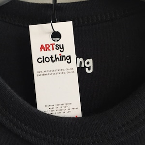 K&ouml;nnte beinhalten: Ein wei&szlig;es Etikett mit schwarzem Text, der "ARTSY clothing" und "WWW.ARTSYCLOTHING.CO.UK" und "INFO@ARTSYCLOTHING.CO.UK" lautet. Das Etikett ist an einem schwarzen T-Shirt befestigt, auf dem das Wort "ing" aufgedruckt ist.