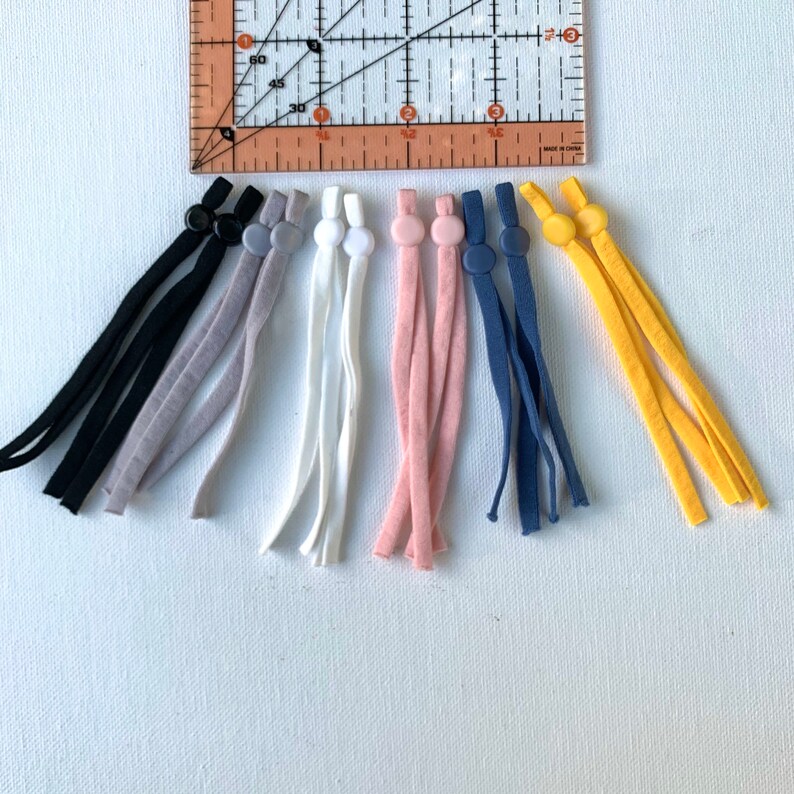 May include: Set of eight colorful elastic mask strap extenders with adjustable toggles. The extenders are in black, gray, white, pink, blue, and yellow.