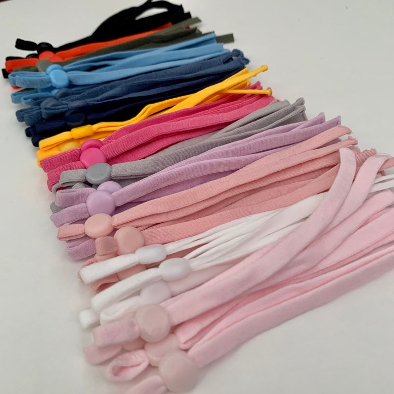 May include: A collection of colorful fabric mask extenders with adjustable plastic slider buttons. The extenders are in various colors, including black, red, orange, green, blue, yellow, pink, purple, gray, and white.