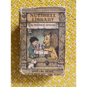 May include: A vintage "Nutshell Library" book by Maurice Sendak. The cover features a boy and a lion reading at a table, with a small dog. The book is in a rectangular shape with the words "Nutshell Library" at the top.