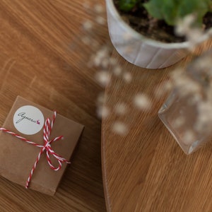 May include: A small brown gift box tied with red and white twine. The box has a white sticker with the word "Agnecia" written on it.