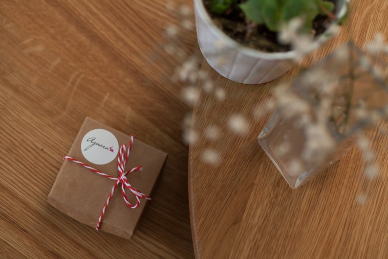 May include: A small brown gift box tied with red and white twine. The box has a white sticker with the word "Agnecia" written on it.