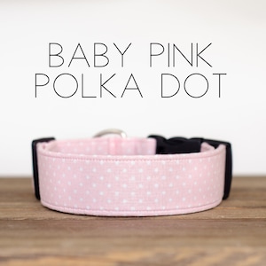 May include: A pink dog collar with white polka dots. The collar has a black buckle and is made of fabric.