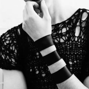 May include: A black and white photo of a person wearing a black crochet top with a black leather bracelet with white stripes.