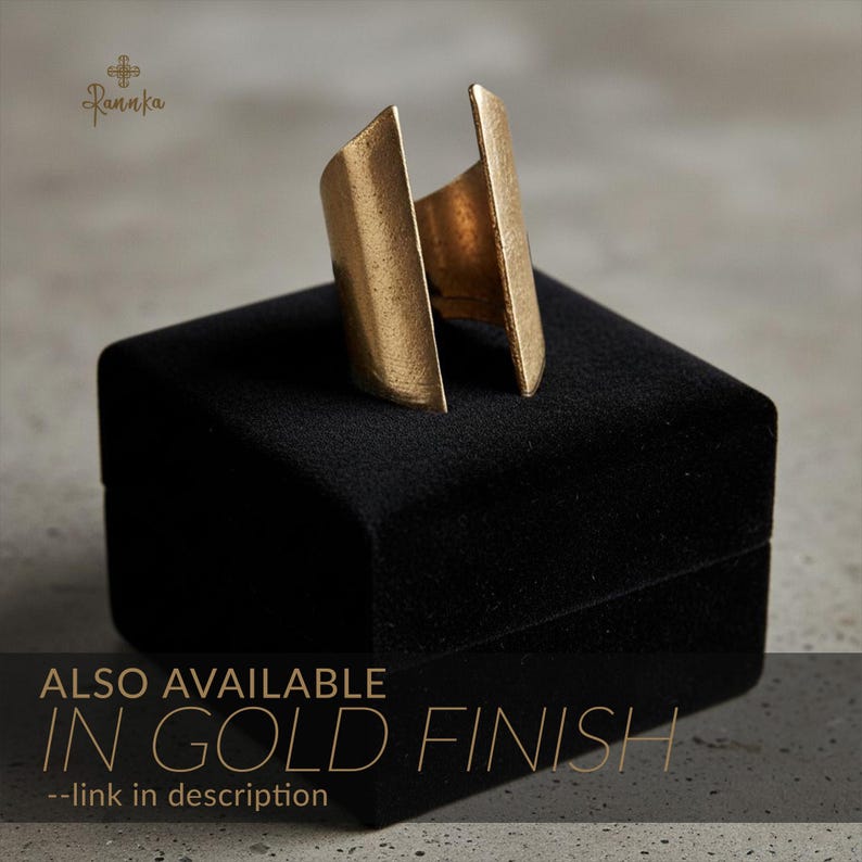Gold statement ring with a geometric open-ended design displayed on a black velvet jewelry box, emphasizing its brushed metallic finish and sculptural form in soft natural light.