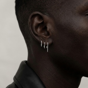 Minimalist sterling silver slip earrings on ear, small and medium bar drop earrings in stacked piercing styling, modern asymmetric ear stack, clean industrial jewelry look, subtle everyday silver earrings, close-up ear with multiple piercings, Rannka style, sleek and understated mood
