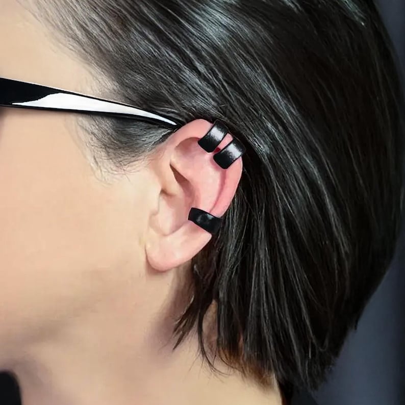 Black ear cuff for men and women in an adjustable design, worn as a no-pierced conch wrap. This edgy minimalist punk earring clip features a smooth black band style that wraps securely around the ear without the need for piercing. A versatile piece of ear jewelry that makes a bold girlfriend birthday gift or statement accessory for everyday wear.