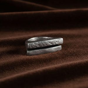 Geometric silver bar ring with a hand-hammered texture, photographed on soft brown fabric. The split-band design gives it a raw, modern edge. Minimalist and gender-neutral piece for everyday wear or gifting. Rannka handcrafted jewelry.