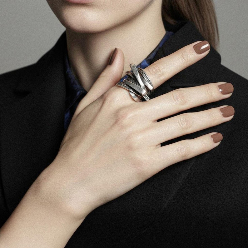 Hand adorned with a bold multi-band silver ring featuring layered twisted forms and oxidized bead details. The jewelry piece contrasts elegantly with a dark tailored blazer, creating a refined yet edgy look. Modern handcrafted statement ring by Rannka.