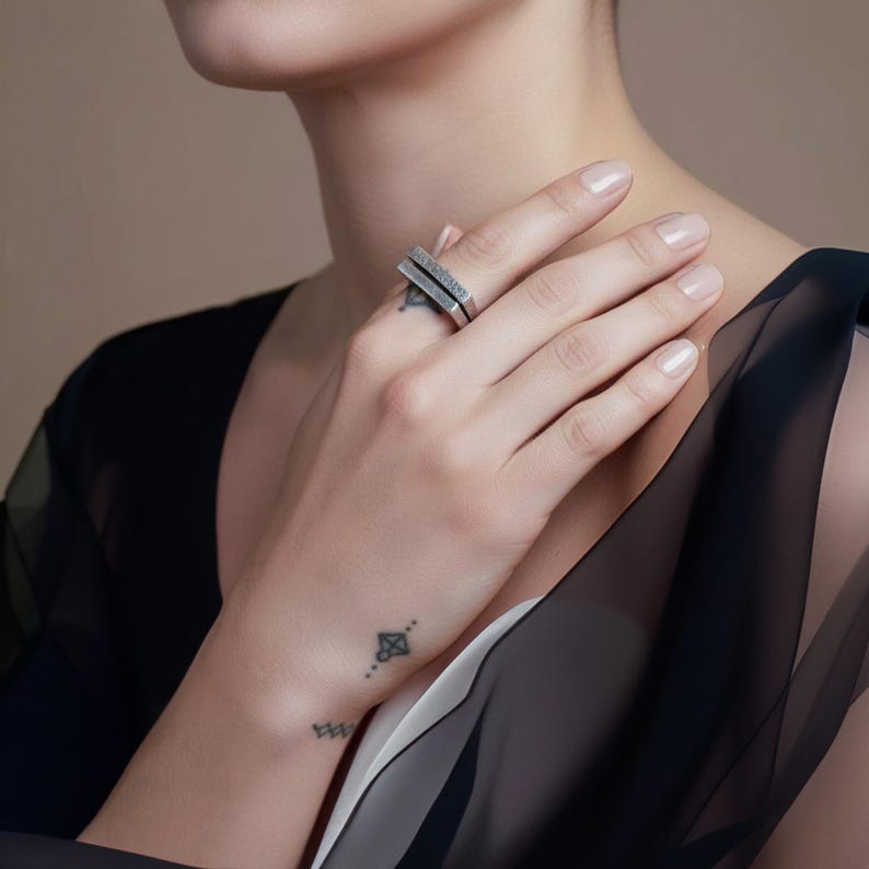 Person wearing a geometric silver bar ring with a textured surface, styled with a sheer black and white top. Minimalist modern jewelry that pairs well with clean, architectural fashion. Elegant everyday or statement piece by Rannka.