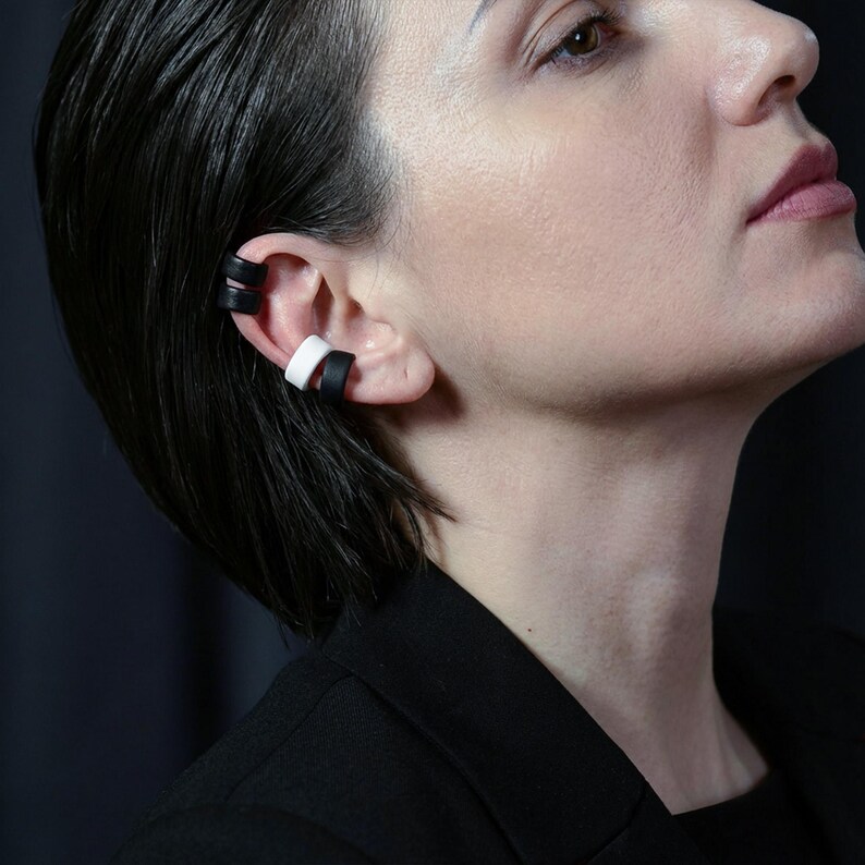 Black and white ear cuff set styled across upper and lower ear, no piercing ear accessories worn layered on ear, matte ear wraps creating a stacked ear look, modern graphic ear jewelry on model profile, clean contemporary styling by Rannka.