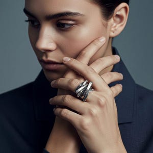 Close-up portrait of a woman wearing a dark blazer, showing her hand adorned with multiple sculptural silver rings. The jewelry features overlapping, leaf-like blade forms with a textured matte finish. Modern, architectural, and minimal styling in soft lighting, consistent with Rannka’s aesthetic.