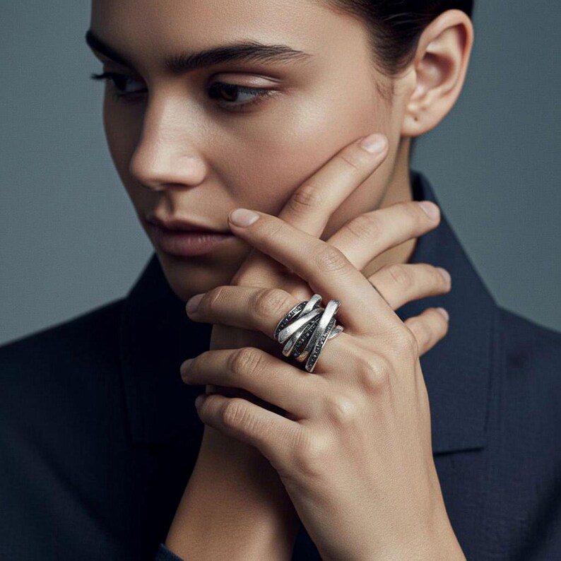 Close-up portrait of a woman wearing a dark blazer, showing her hand adorned with multiple sculptural silver rings. The jewelry features overlapping, leaf-like blade forms with a textured matte finish. Modern, architectural, and minimal styling in soft lighting, consistent with Rannka’s aesthetic.