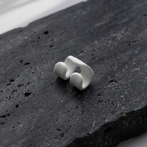 White ear cuff worn without piercings, sculptural no hole ear jewelry displayed on textured stone surface, minimalist ear accessory with smooth matte finish, modern ear wrap design for stacking and layering, contemporary handmade ear jewelry by Rannka.