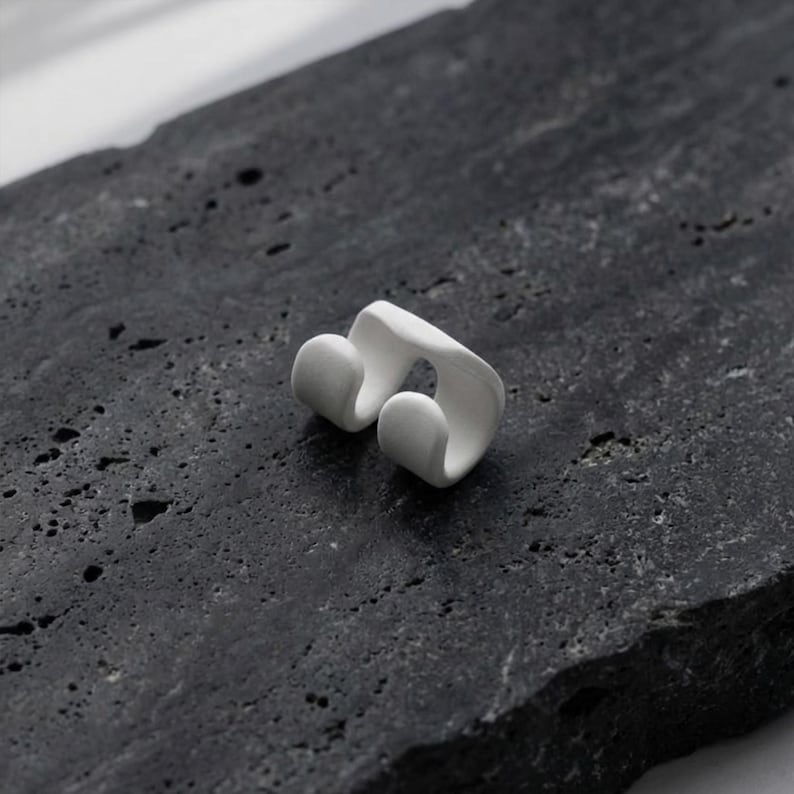 White ear cuff worn without piercings, sculptural no hole ear jewelry displayed on textured stone surface, minimalist ear accessory with smooth matte finish, modern ear wrap design for stacking and layering, contemporary handmade ear jewelry by Rannka.