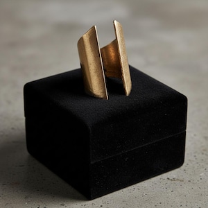 Gold geometric open-band ring displayed on a black velvet jewelry box, photographed on a neutral concrete surface with soft natural light, highlighting its bold sculptural shape and refined minimalist design by Rannka.