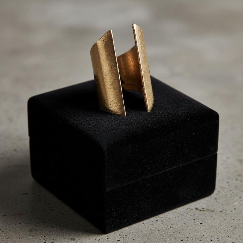 Gold geometric open-band ring displayed on a black velvet jewelry box, photographed on a neutral concrete surface with soft natural light, highlighting its bold sculptural shape and refined minimalist design by Rannka.