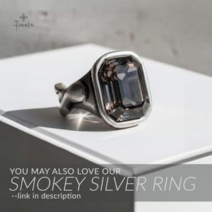 May include: Smokey silver ring with a large, rectangular, dark gray gemstone. The ring has a silver-tone band and setting. The image includes the text "YOU MAY ALSO LOVE OUR SMOKEY SILVER RING --link in description."
