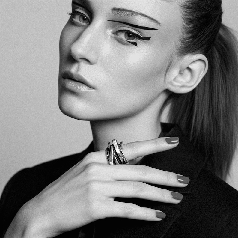 Black and white portrait of a woman wearing a layered oxidized silver ring with intersecting bands and dotted texture. Styled with graphic eyeliner and a tailored black jacket, the photo captures a bold modern aesthetic. Artistic editorial jewelry image by Rannka.
