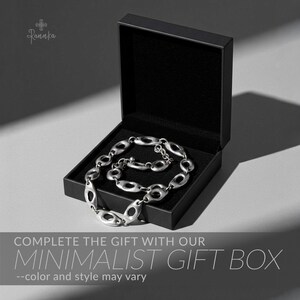 Peut inclure: Un collier argent&eacute; &agrave; maillons ovales est pr&eacute;sent&eacute; dans un coffret cadeau noir ouvert, doubl&eacute; de tissu noir. Le texte "COMPLETE THE GIFT WITH OUR MINIMALIST GIFT BOX" est affich&eacute; en dessous.