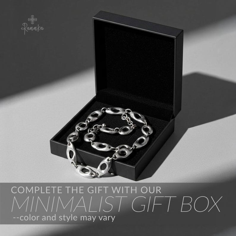 Peut inclure: Un collier argent&eacute; &agrave; maillons ovales est pr&eacute;sent&eacute; dans un coffret cadeau noir ouvert, doubl&eacute; de tissu noir. Le texte "COMPLETE THE GIFT WITH OUR MINIMALIST GIFT BOX" est affich&eacute; en dessous.