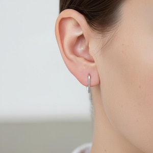 Sterling silver slim hook earring worn in single piercing, minimal curved wire earring with straight drop, lightweight everyday ear wire, clean refined silver jewelry, subtle modern look, close-up ear detail, understated minimalist styling, Rannka aesthetic