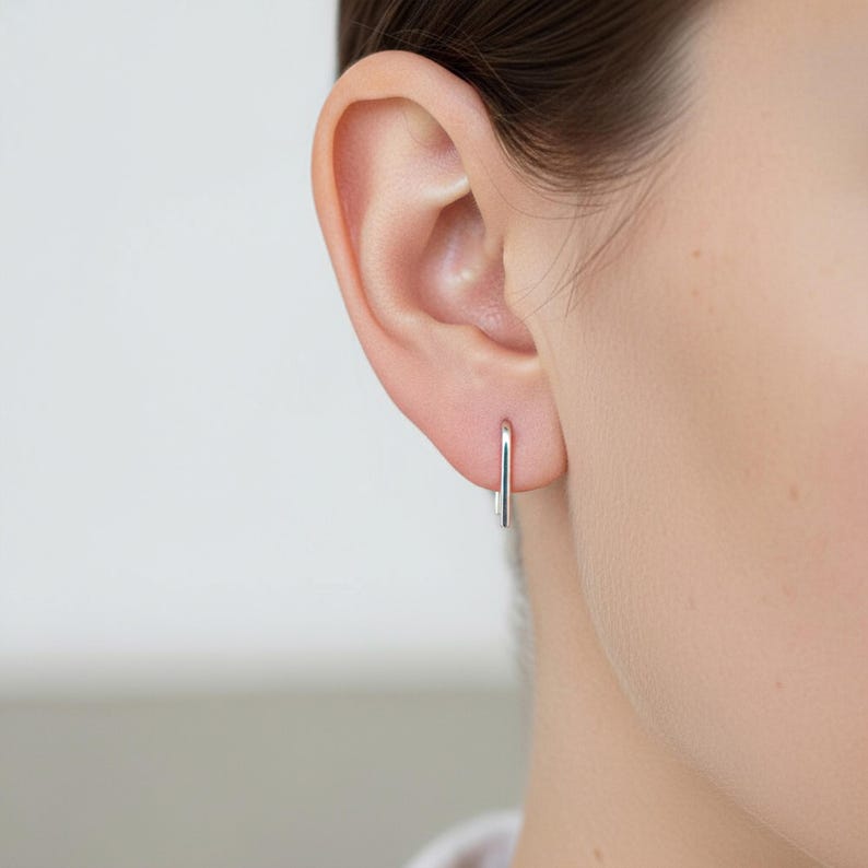 Sterling silver slim hook earring worn in single piercing, minimal curved wire earring with straight drop, lightweight everyday ear wire, clean refined silver jewelry, subtle modern look, close-up ear detail, understated minimalist styling, Rannka aesthetic
