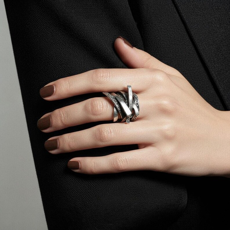 Close-up of a hand wearing a layered oxidized silver ring with intersecting textured bands and dotted details. The ring rests against a black tailored sleeve, combining sculptural design with modern elegance. Artisan statement jewelry by Rannka.