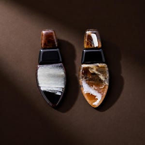 May include: A pair of drop earrings featuring a three-part design. The top section is a brown tortoiseshell rectangle, the middle is a solid black rectangle, and the bottom is a large, pointed teardrop shape with marbled white and black patterns.