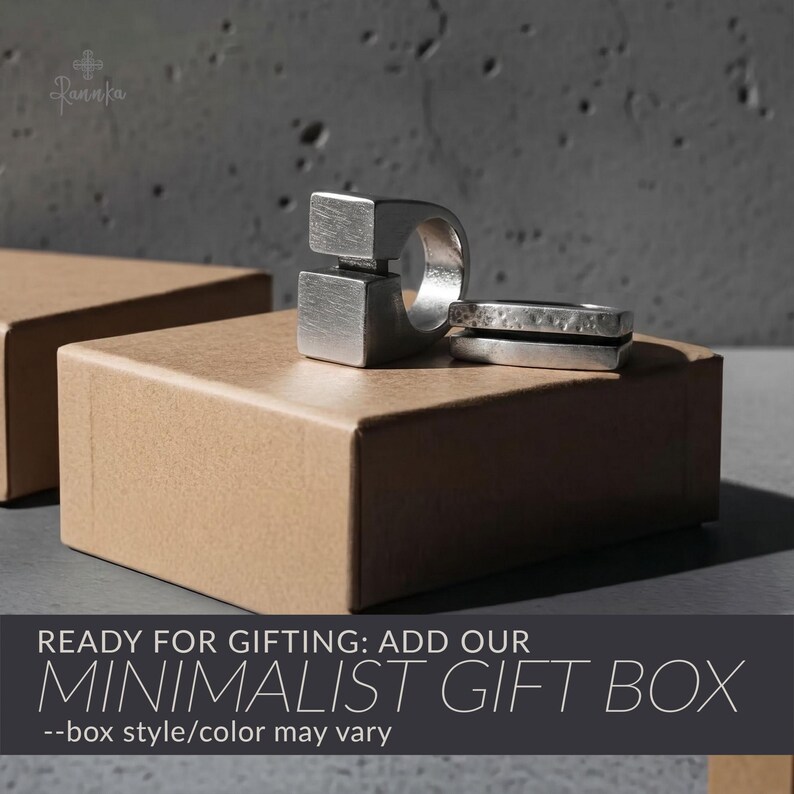 May include: Two silver rings with geometric designs rest on a brown gift box. One ring features a square design, while the other has a textured band. The image includes the text "READY FOR GIFTING: ADD OUR MINIMALIST GIFT BOX".
