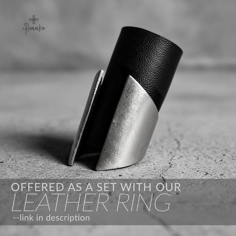 Silver geometric statement ring paired with a black vegan leather band, photographed on a textured concrete surface — highlighting contrast, craftsmanship, and modern design synergy.