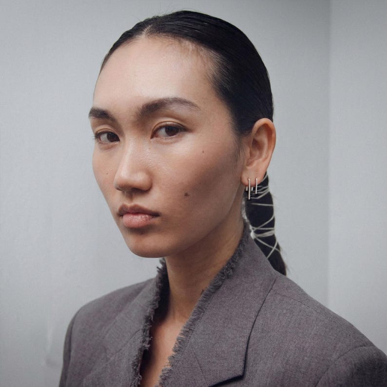 Sterling silver ear threader set in double piercing, slim curved wire earrings with vertical drop, modern minimalist ear stack styling, lightweight pull through earrings, clean geometric silver jewelry, subtle everyday look, portrait styling with tailored blazer, Rannka aesthetic