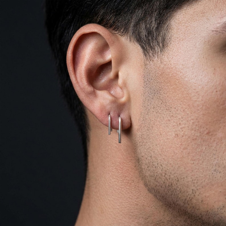 Sterling silver arc drop earrings in double piercing, sleek U shaped ear wires with straight tails, modern minimal ear styling, refined geometric silver earrings, lightweight everyday jewelry, close-up ear with textured skin detail, clean contemporary look, Rannka aesthetic