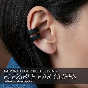 May include: A matte black double-band ear cuff worn on the upper cartilage. The image includes the text: PAIR WITH OUR BEST SELLING FLEXIBLE EAR CUFFS --link in description. The accessory features a smooth, solid finish and a simple, open-loop design.
