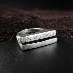 Geometric Silver Ring, Hammered silver ring with a split front design, raw textured surface and geometric form, photographed against a dark backdrop with earthy tones, contemporary brutalist jewelry by Rannka.