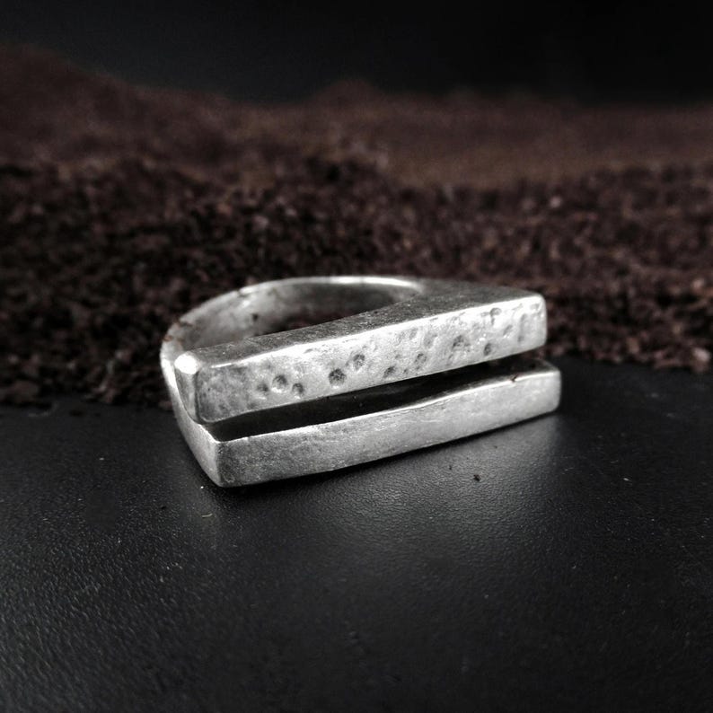 Geometric Silver Ring, Hammered silver ring with a split front design, raw textured surface and geometric form, photographed against a dark backdrop with earthy tones, contemporary brutalist jewelry by Rannka.