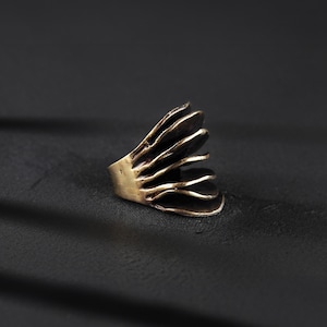 extra large gold ring with organic design resting on the dark surface with strong shadow in the background