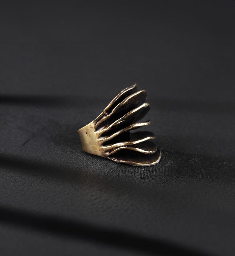 extra large gold ring with organic design resting on the dark surface with strong shadow in the background