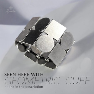 May include: Silver geometric cuff bracelet with a repeating pattern of shapes, including squares, circles, and rectangles. The bracelet is made of metal and has a flexible design. The text on the image says "SEEN HERE WITH GEOMETRIC CUFF -- link in the description."