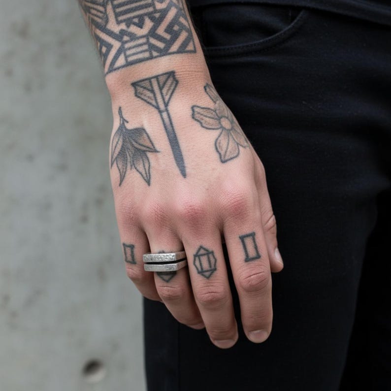 Tattooed hand wearing a hammered geometric silver bar ring. The ring’s raw, split-bar form stands out against black clothing, blending industrial edge with minimalist design. Unisex modern jewelry for everyday wear. Rannka handcrafted piece.