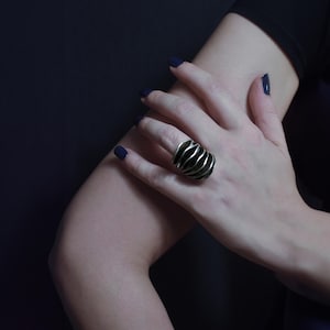 Large Statement silver ring on women's hand resting on her elbow. dark background and elegant styling